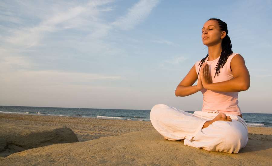 Personne méditant en position du lotus sur la plage, effectuant un exercice de respiration consciente pour se détendre et équilibrer le corps et l’esprit.