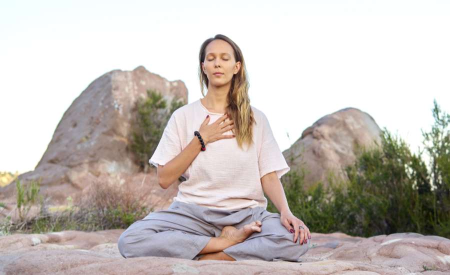 Femme en plein air, assise en tailleur, combinant méditation et respiration consciente pour une détente profonde et une meilleure oxygénation.